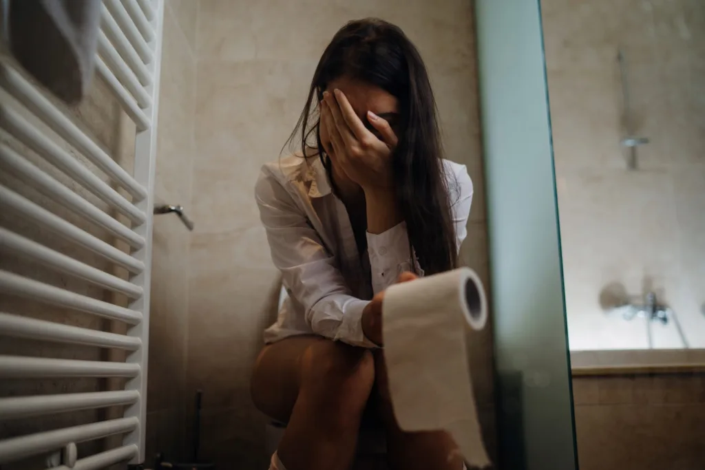 Woman sitting on the toilet, sad, embarrassed. IBS dietitian in California and Europe